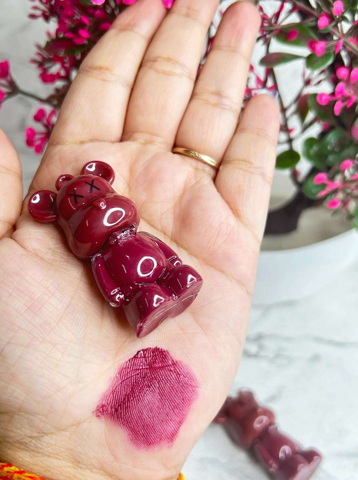 Cute bear-shaped long lasting lip tint set in burgundy shade on a hand with floral background